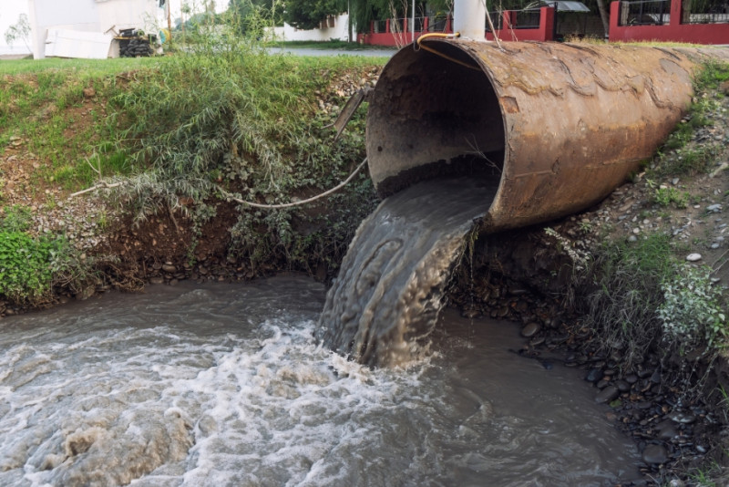 Pipe with visibly dirty water puring out into a small hole containing more dirty water