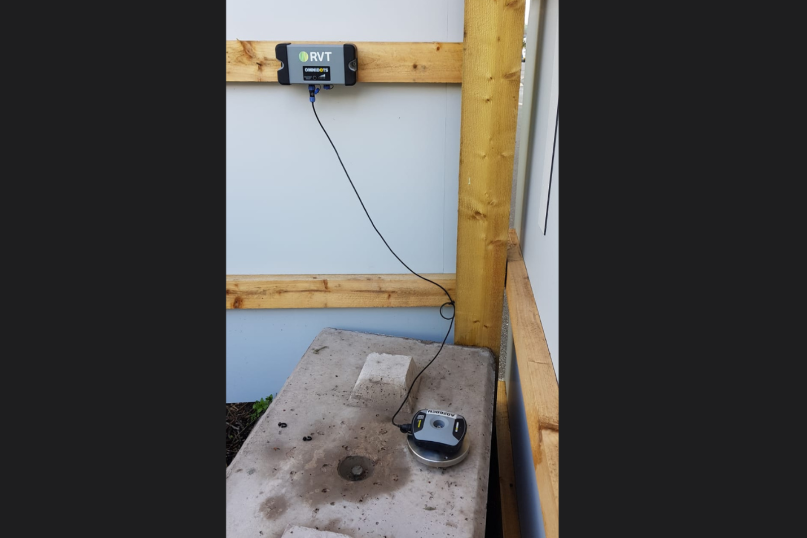 Close up of a MONITEX OD-AA Vibration Monitor with one part on a large stone slab and one part on an adjoining fence