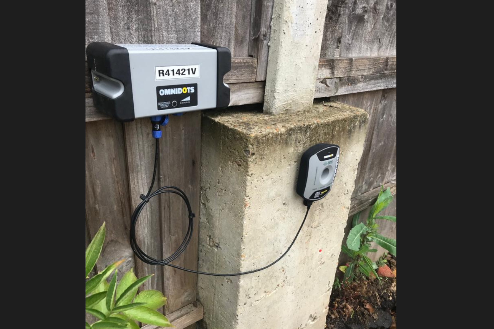 Close up of a MONITEX OD-AA Vibration Monitor with one part on a stone slab and one part on an adjoining fence