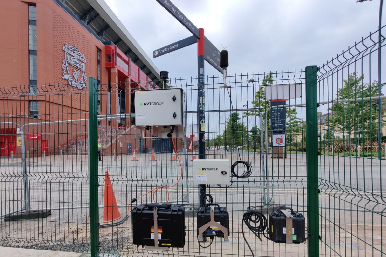 MONITEX noise monitor and power packs mounted to a fence with Liverpool football stadium in the background
