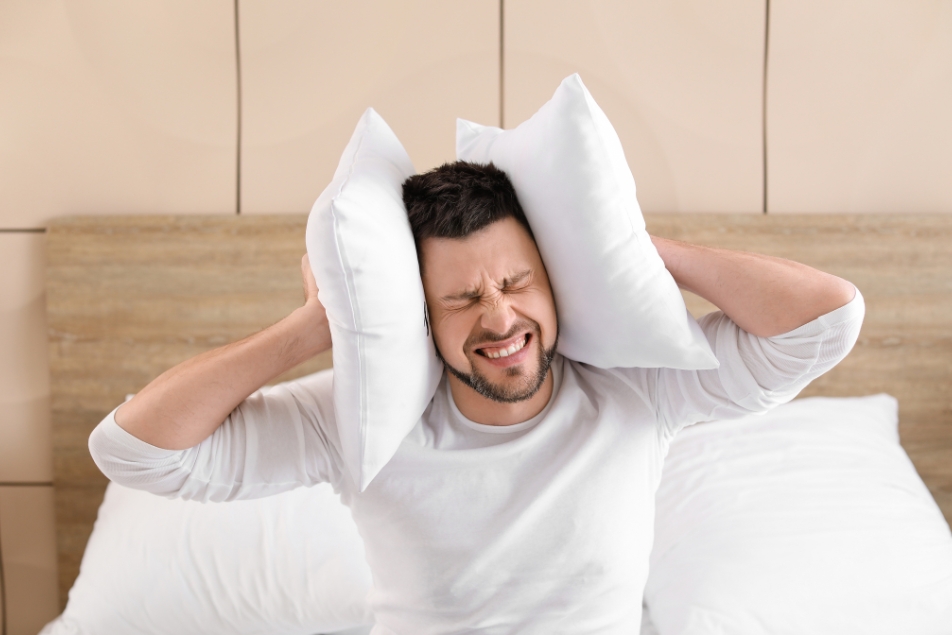 Man blocking ears with pillows