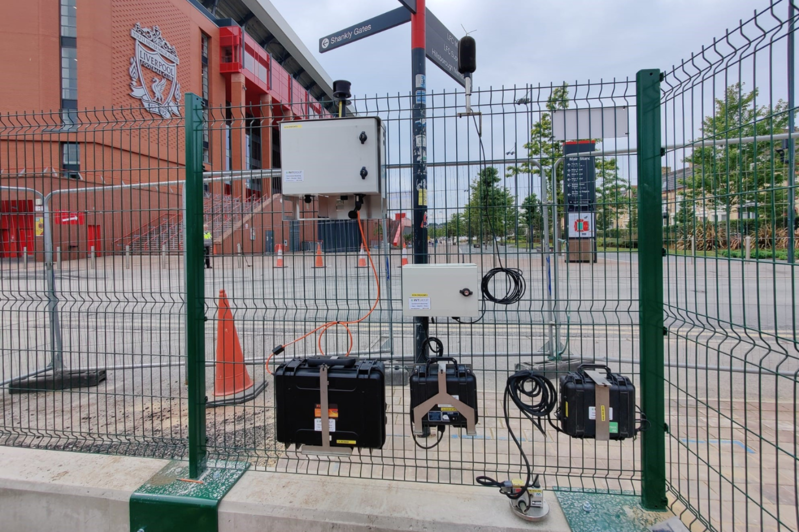 Monitex dust, noise and vibration monitoring on a fence with liverpool football stadium in the background