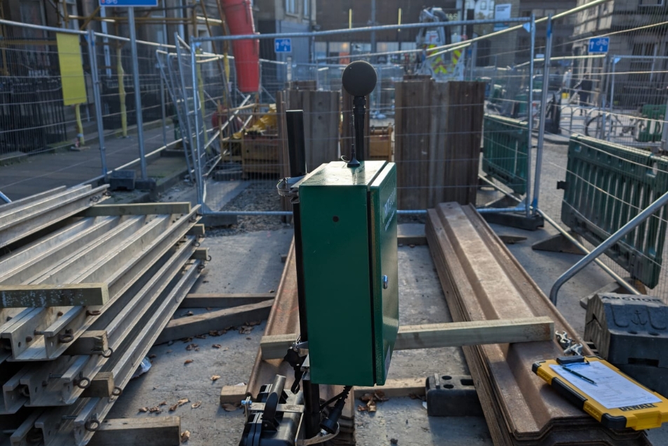 Noise monitor in foreground with construction materials and site in the background