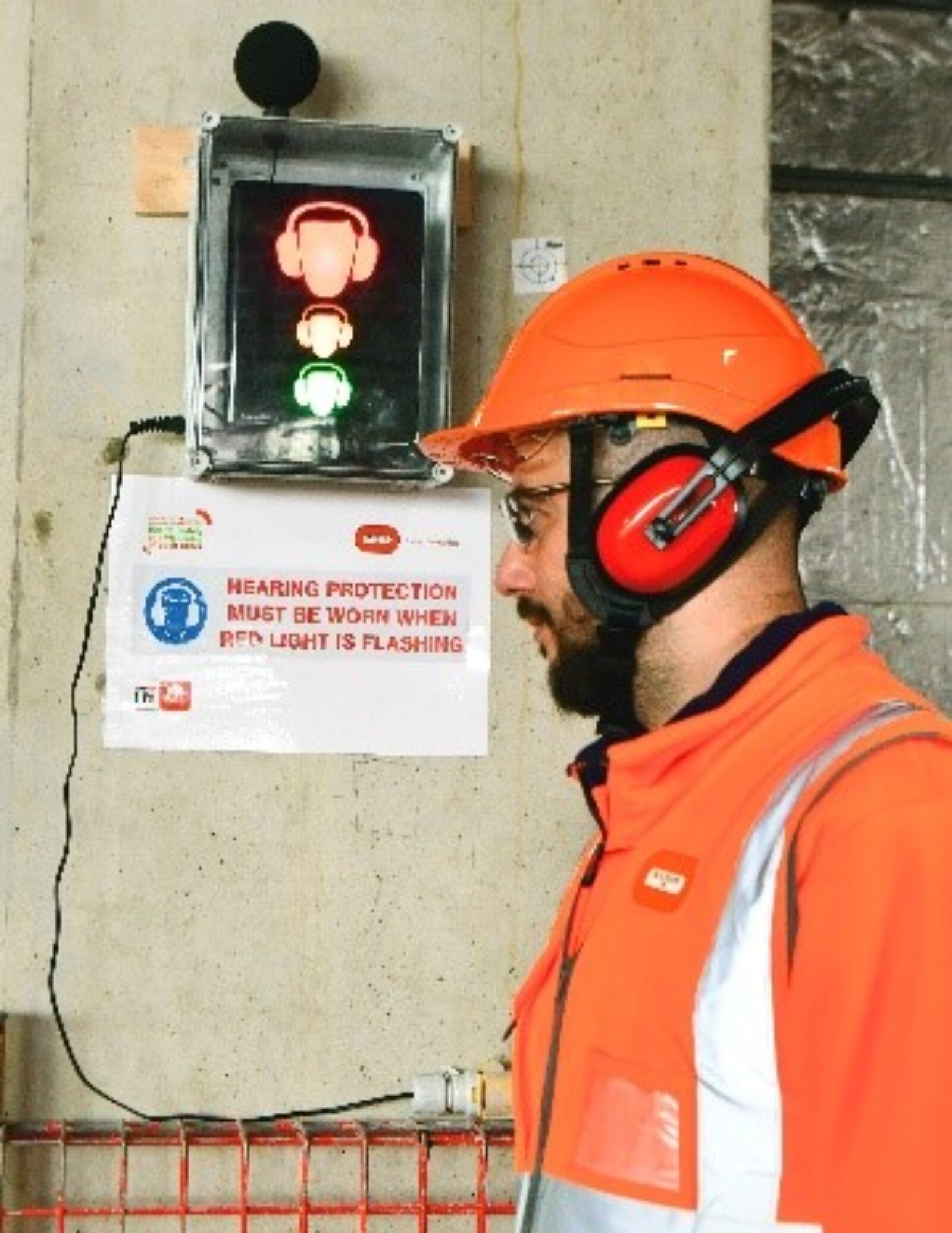 Portable Noise Level Warning System next to worker with ear protection and full orange overall PPE