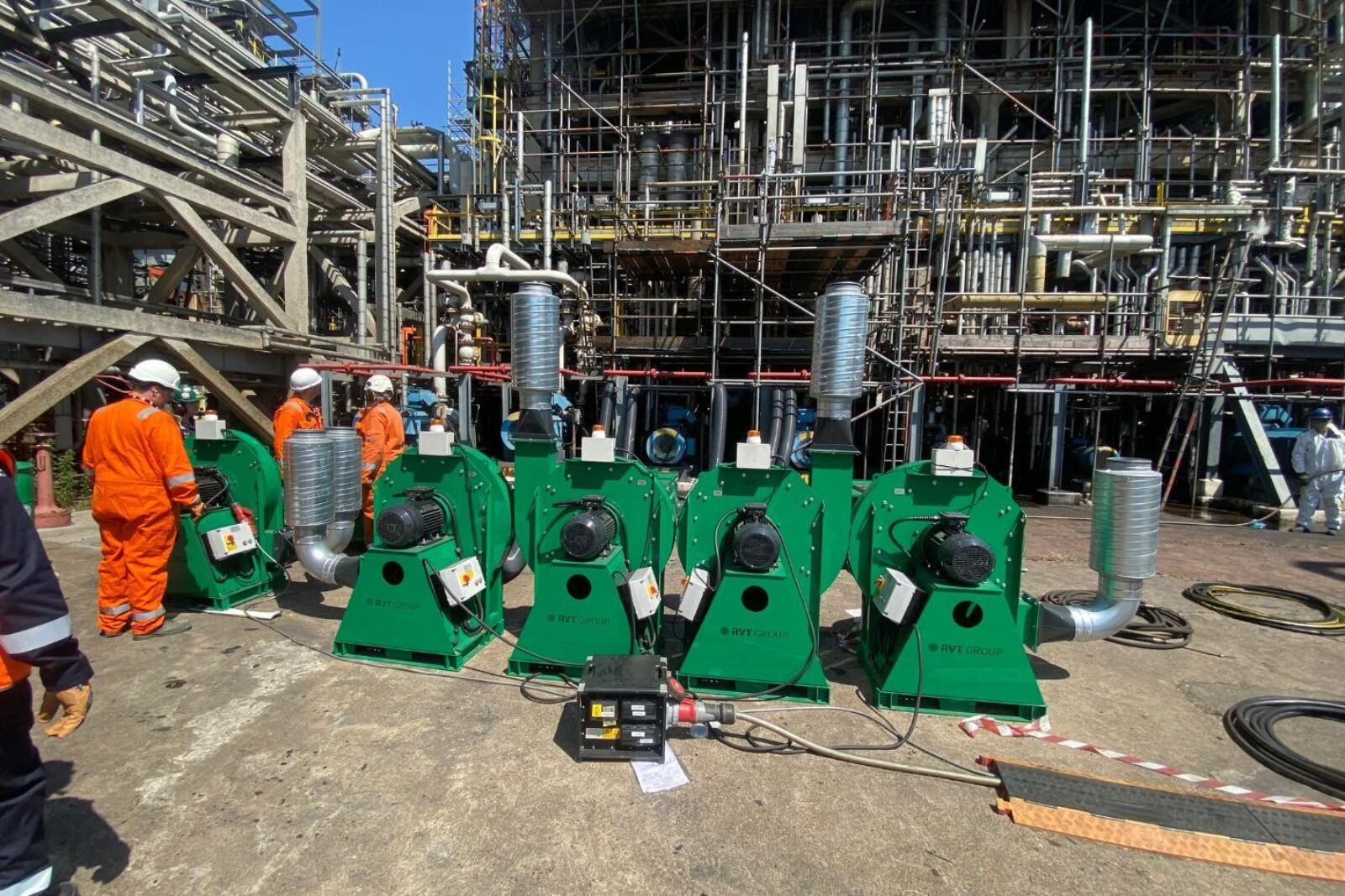 Several VENTEX Centrifugal Fan 200S-HPs making up part of a number of fume extraction systems on the floor with pipework entering an oil refinery and 3 workers in orange hi-vis overalls nearby