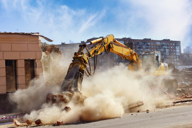 demolition with an excavator creating airborne dust
