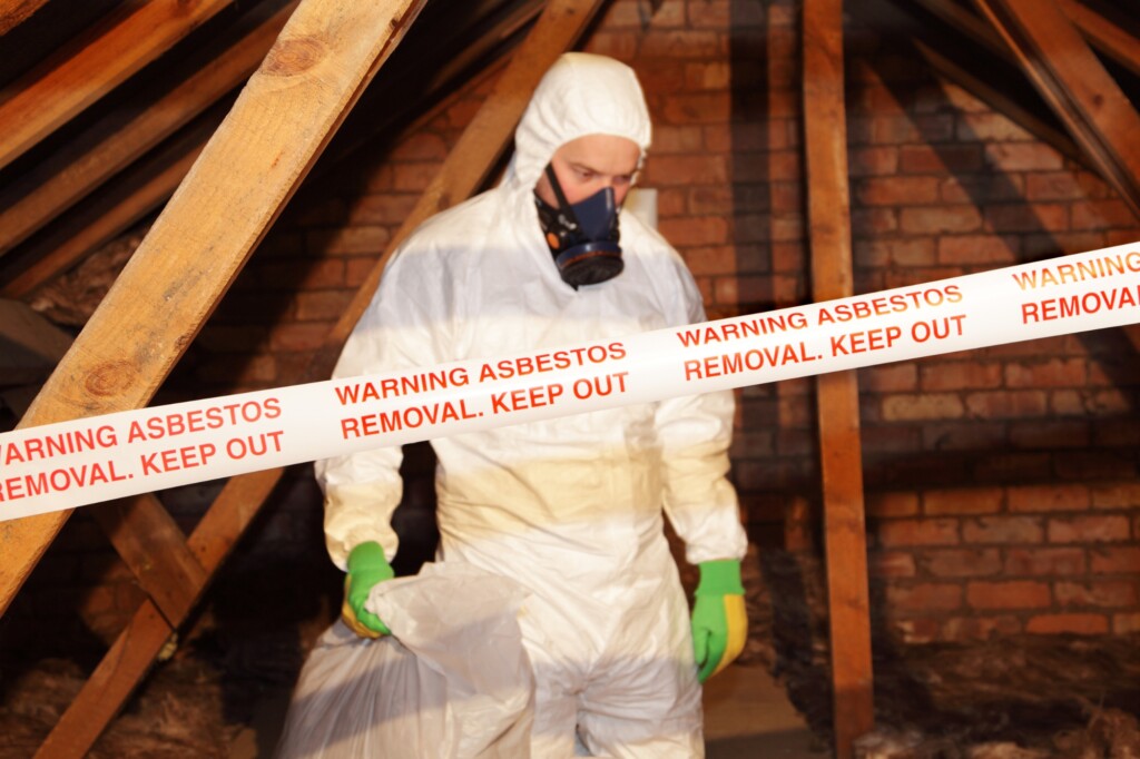 person in overalls, mask and gloves with asbestos removal warning tape